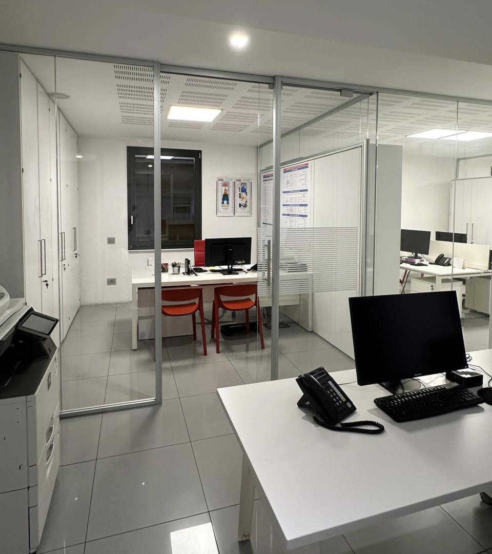 Ufficio moderno con arredi bianchi, scrivanie, computer e sedie rosse.